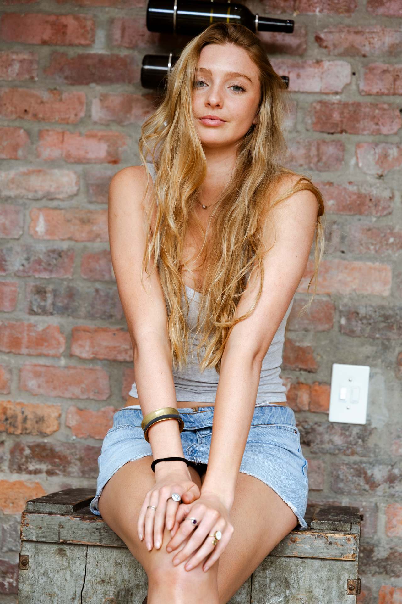 Digitals mid length: Georgia Bauriedl seated against a brick wall in a grey vest and denim.