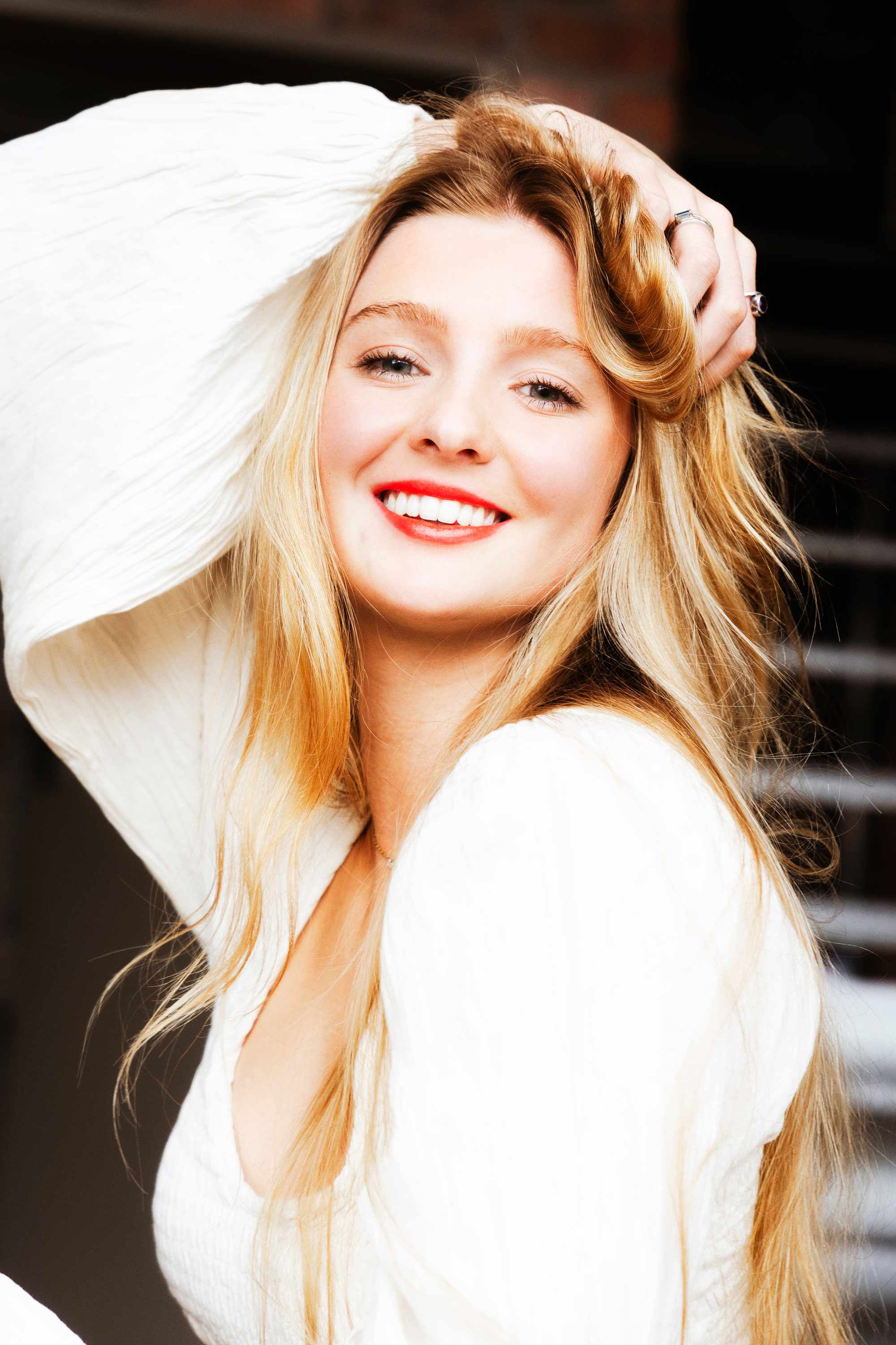 Georgia Bauriedl laughing in a white shirt with a bold red lip, hand lifting her hair.